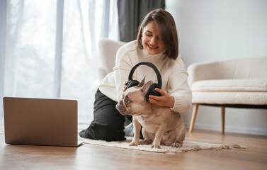 Headphones on the head. With laptop. Young woman is with her pug dog at home