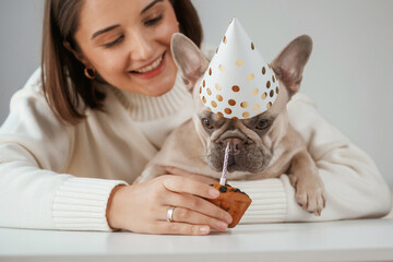 Happy birthday. Pet in hat and with cake. Young woman is with her pug dog at home