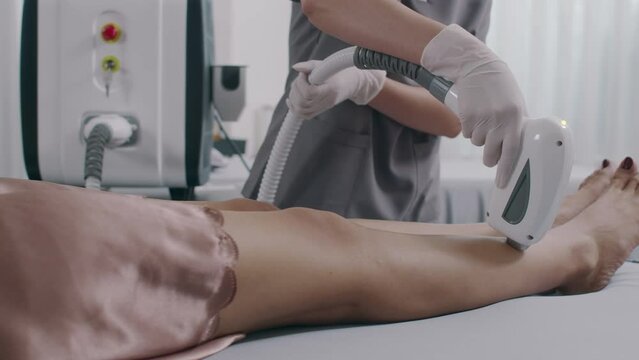 Cropped shot of unrecognizable beauty salon specialist removing hair on clients legs with laser equipment