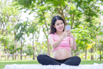 Asian pregnant woman using a smartphone talking on a video call, Young Asian woman relaxing in the...