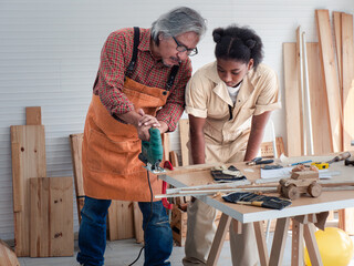Teenaged girls learn to use an electronic saw and play with their grandfather in the wooden workshop, a concept for enhancing the development and thinking of children.