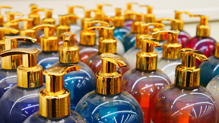 Close-up of many beautiful colorful bottles of perfume gel with golden dispenser caps standing in...