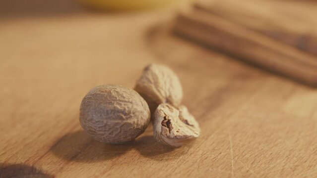 Whole dried nutmeg seed with defocused cinnamon in the background on a wooden rustic table. Handheld. Slow motion. Close up. Interior, kitchen. Studio shot. High quality 4k footage
