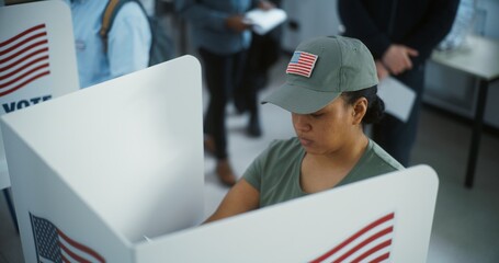 Female American army soldier votes in booth in modern polling station office. National Election Day in United States. Political races of US presidential candidates. Civic duty and patriotism concept. - obrazy, fototapety, plakaty