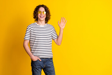 Photo of nice young man arm wave hello empty space wear striped t-shirt isolated on yellow color...