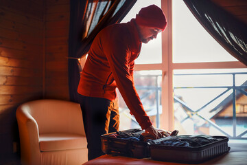 Stylish hipster traveller man in red hat in wooden house packing suitcase