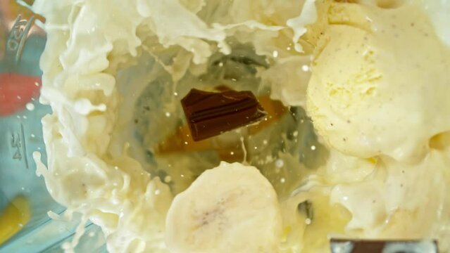 Super slow motion of mixing pieces of ice cream and chocolate in blender with milk, camera movement, top shot. Filmed on high speed cinema camera, 1000 fps.