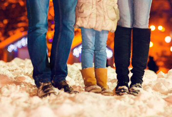 Feets of a family wearing winter shoes on the snow over Christmas lights