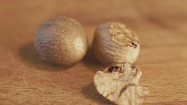 Woman hand touching whole dried nutmeg seed on a wooden rustic table. Handheld. Slow motion. Close up. Interior, kitchen. Studio shot. High quality 4k footage