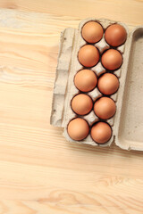 Chicken eggs in a cardboard box, top view. Eggs on a wooden background. Ten fresh raw eggs. Brown chicken eggs in a recycled cardboard tray on a wooden table