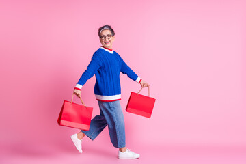 Full body profile portrait of nice aged lady hold bags walk empty space wear blue sweater isolated on pink color background - obrazy, fototapety, plakaty