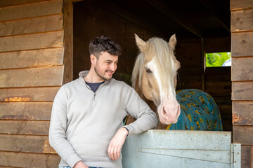 Man with a horse, Image shows a 28 year old bearded male posing with a palomino section D Welsh cob pony, stallion in it's stable on a small farm in Surrey - obrazy, fototapety, plakaty