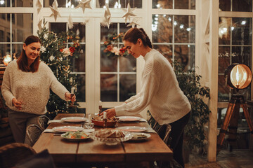 Mother and daughter setting festive Christmas table together at cozy decorated rustic farmhouse