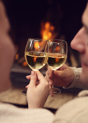 Romantic young couple toasting wineglasses in front of lit fireplace