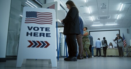 Vote here sign on the floor. Multi ethnic American citizens vote in booths in polling station...