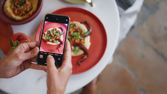 Woman hands taking photos of tasty dinner using mobile phone at restaurant table