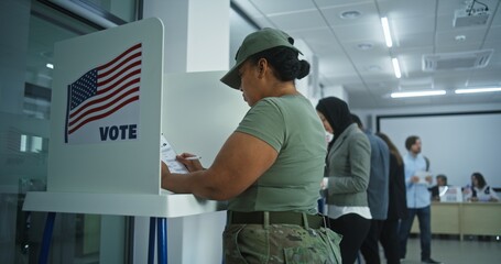 Female American army soldier votes in booth in polling station office. National Elections Day in the United States. Political races of US presidential candidates. Concept of civic duty. Dolly shot. - obrazy, fototapety, plakaty