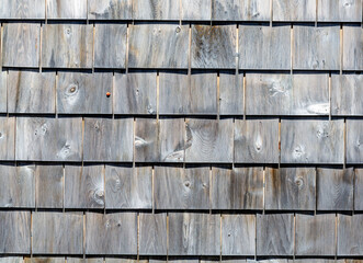 Several rows of weathered gray cedar shingles in morning light close view.