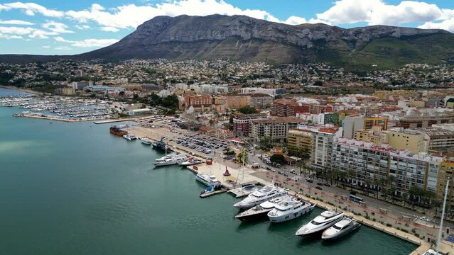 4k Panoramic aerial view of Denia city and part of the port. Drone forward above the marina of the city. Luxury yachts docked. View of promenade area of the city. Travel destination in Spain.