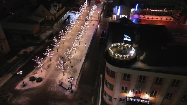 Estonian flag on Tower in the the city of Voru, Estonia. Beautiful winter landscape with Estonia flag waving in the wind. Christmas lights flickering in the background. Christmas holiday