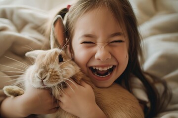 Adorable young girl laughing with delight as she cuddles a soft, brown rabbit at home