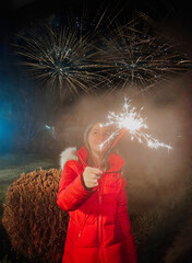 Happy girl holding sparkler while celebrating New Year outdoors in twilight