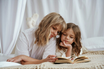 Reading the book together. Mother with daughter are at home - obrazy, fototapety, plakaty