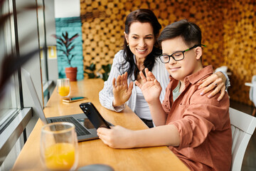 jolly inclusive boy with Down syndrome waving at phone camera on video call near his mother in cafe
