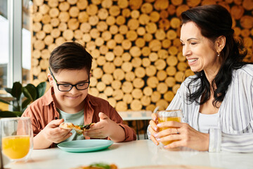 merry mother eating pizza and drinking juice with her inclusive cute son with Down syndrome