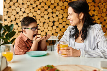 merry mother eating pizza and drinking juice with her inclusive cute son with Down syndrome