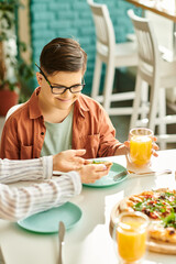 good looking mother eating pizza and drinking juice with her inclusive cute son with Down syndrome