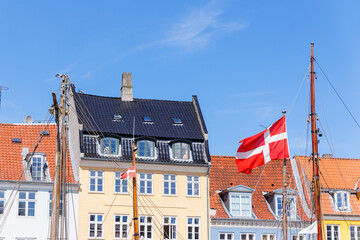Danish flag waves background Nyhavn colorful house buildings in canal harbor Copenhagen sightseeing tourist travel destination in Denmark on sunny day. Clear blue sky backdrop