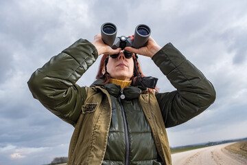 female ornithologist birdman or explorer watches birds with binoculars against a background of a stormy sky
