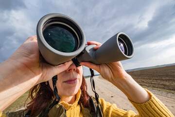 female ornithologist birdman or explorer watches birds with binoculars against a background of a stormy sky