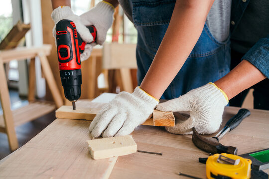 Asian father and son work as a woodworker or carpenters. Close up hands of the father and his son drill holes in a wooden plank carefully together. carpentry working at a home workshop studio.