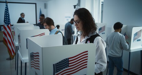 Woman in glasses votes in booth in polling station office. National Election Day in United States....