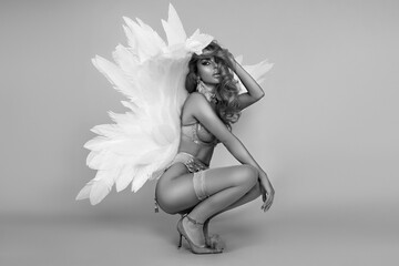 Beautiful sexy blonde woman in elegant lingerie and angel wings is sensually posing in studio....