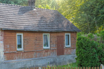 Drewniany opuszczony historyczny ( ponad sto lat) dom we wsi wśród borów. Stary tradycyjny dom z dachem z dachówek betonowych w popołudniowym lipcowym słońcu. © Grzegorz
