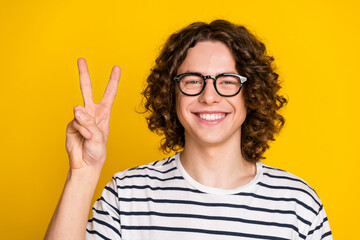 Portrait of teenager curly hair smiling guy wearing striped t shirt make v sign peace symbol...