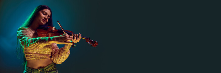 Banner. Talented Indian woman playing violin in neon light against gradient background. with negative space to insert text. Concept of art, music, hobby, classical music and modern lifestyle. Ad