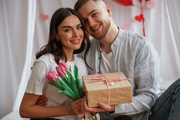 Presents for Valentine's day, gift box and flowers. Young couple are together at home