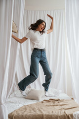 Jumping with pillow. Young beautiful woman is at home on the bed