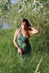 Outdoor portrait of young beautiful woman with long hair against green nature