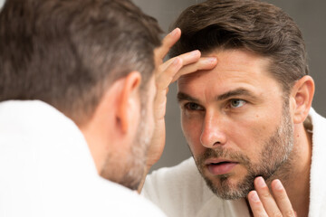 a man in a white bathrobe in the bathroom looking at the skin on his faceSpa male model, skincare...