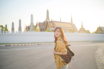 Traveler asian woman in her 30s, backpack slung over her shoulder, explores the intricate details of Wat Pra Kaew with childlike wonder. Sunlight dances on the golden rooftops.