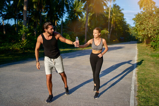 Two persones running. One giving bottle of water to another.