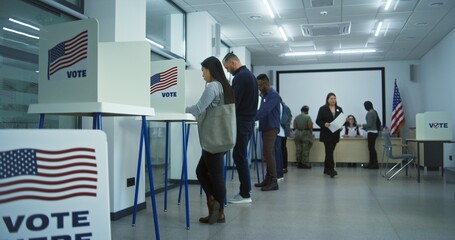 Diverse American citizens vote in booths in polling station office. National Election Day in United States. Political races of US presidential candidates. Civic duty concept. Slow motion. Dolly shot.