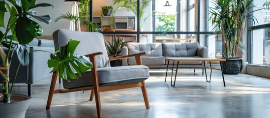 Fototapeta premium Puff and gray armchair situated in a large living room space with plants and a sofa next to a wooden table.