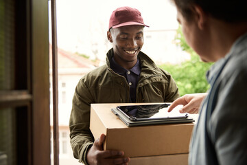 Smiling African courier getting a customer's digital signature for a delivery