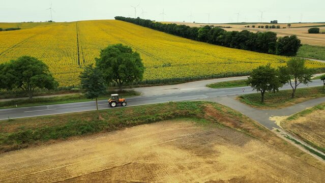 Tractor driving on the road, wet asphalt. Drone shot of tractor driving in the green and yellow field. Leaving work. Spraying the herbicides on the green field is completed.